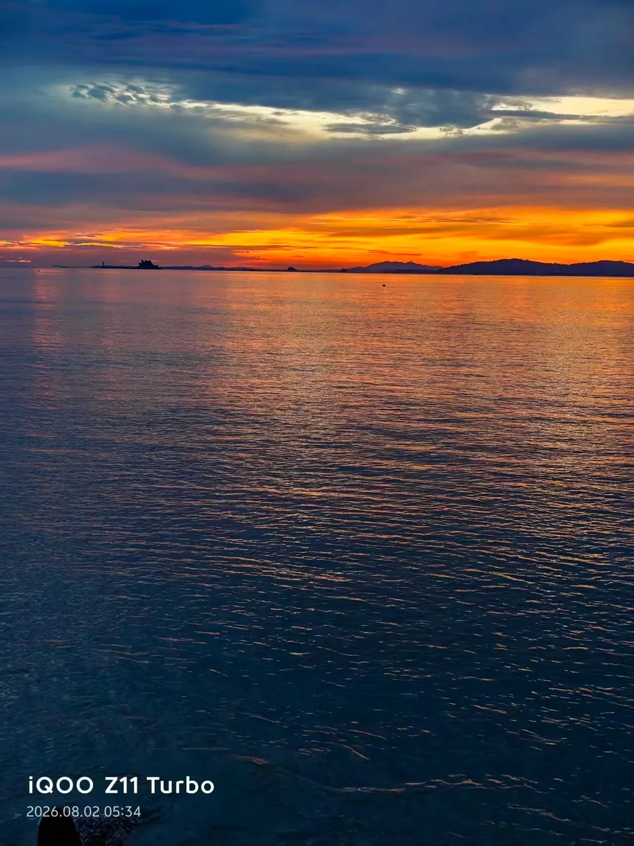 A calm sea under an orange band of cloud just after sunrise in Xiamen