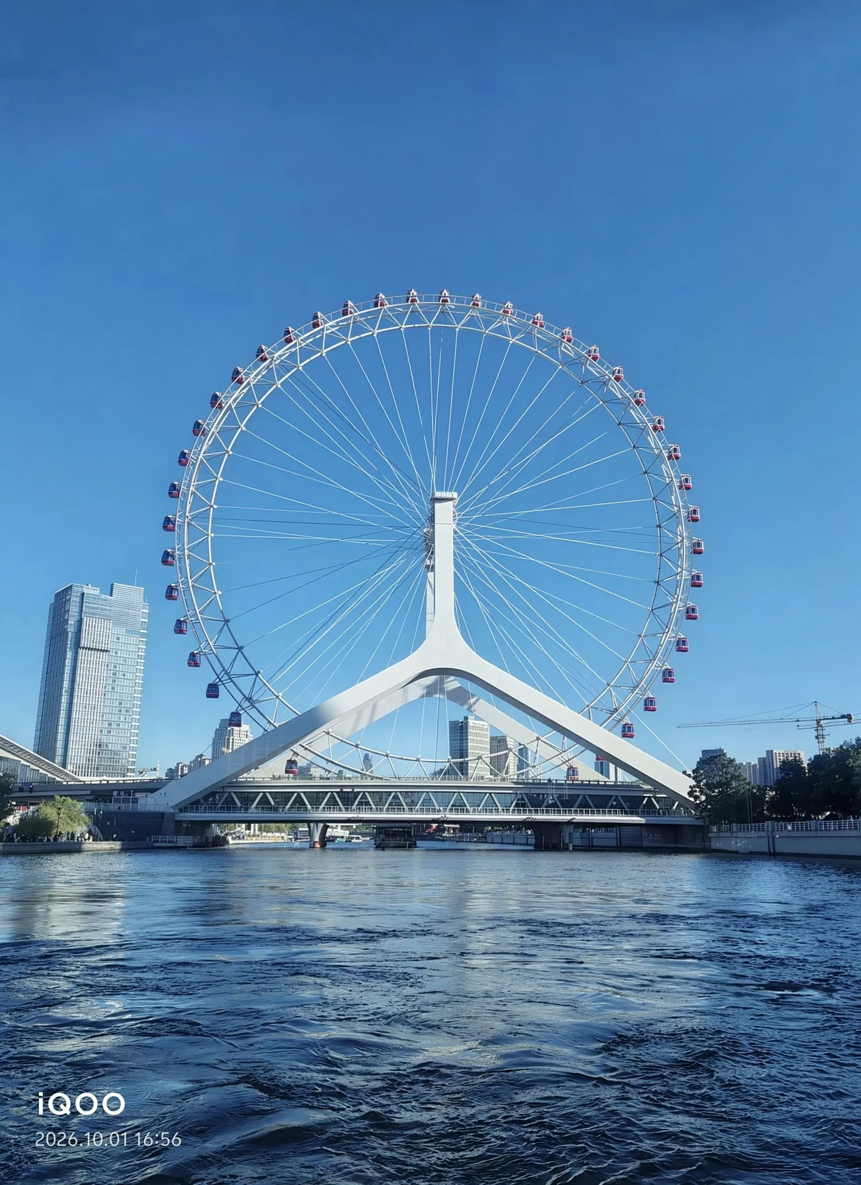 A white ferris wheel spanning the river under a clear blue sky