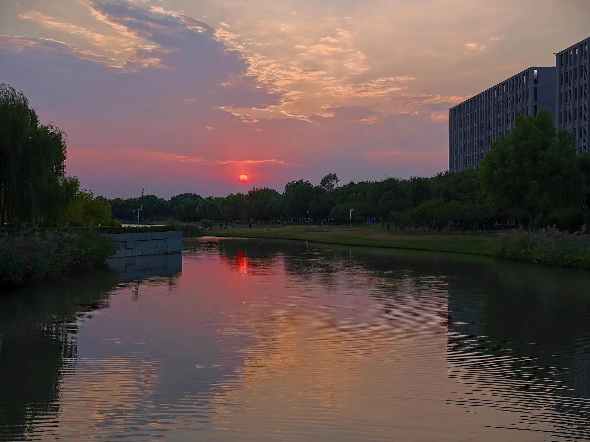 The sun setting behind trees and reflected in a canal on campus